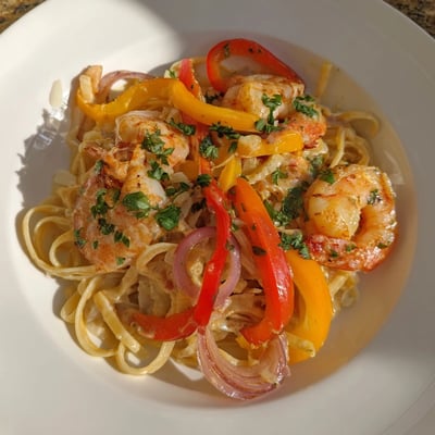 Savory Creamy Cajun Shrimp Pasta with Bell Peppers in a skillet, garnished with fresh parsley and served with lemon wedges for a bright finish.  